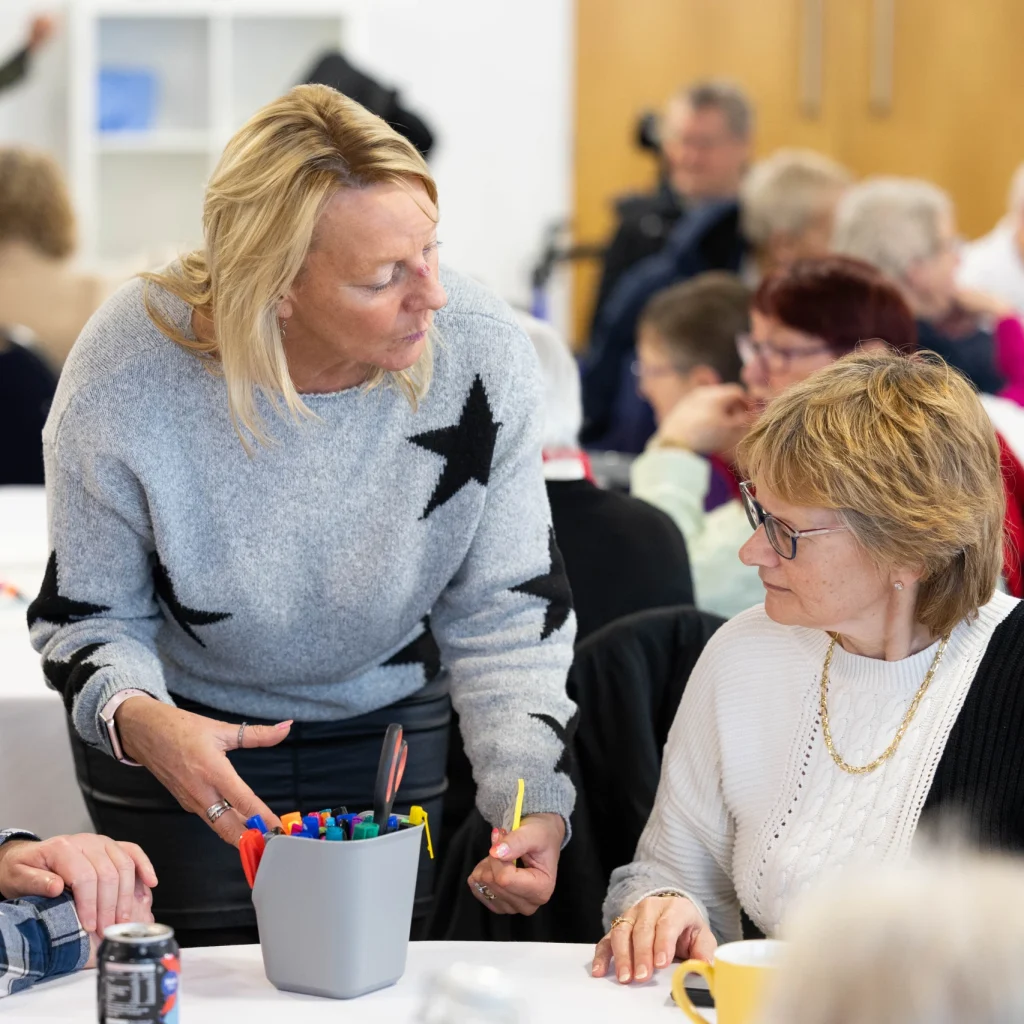 A person standing at a table helping two other people during a busy community activity session.